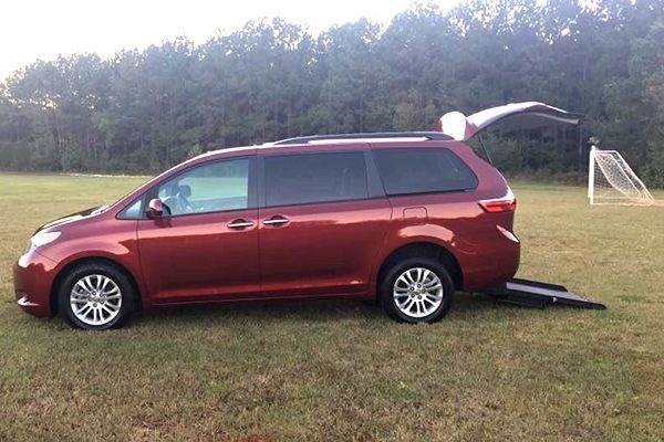 Red accessible minivan with ramp deployed on grassy field. Tailgate and rear door are open.