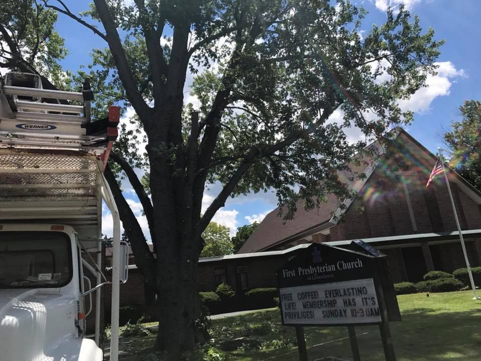 Truck with ladder next to a tree being trimmed near a church. Sign in front of the church.