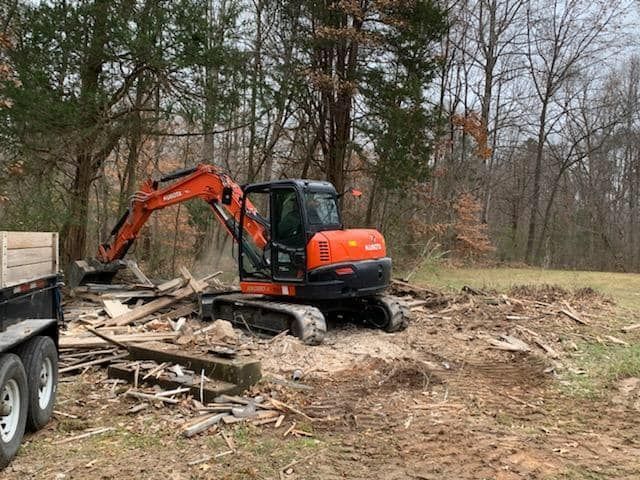 a small excavator is moving a pile of wood in a field .