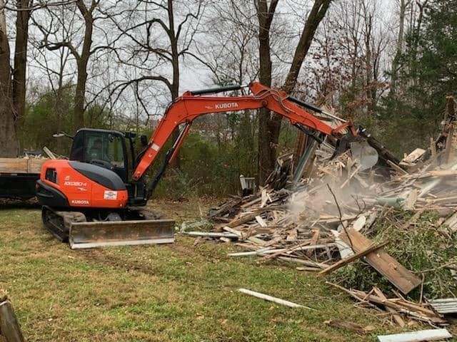 an excavator is demolishing a house in a yard .
