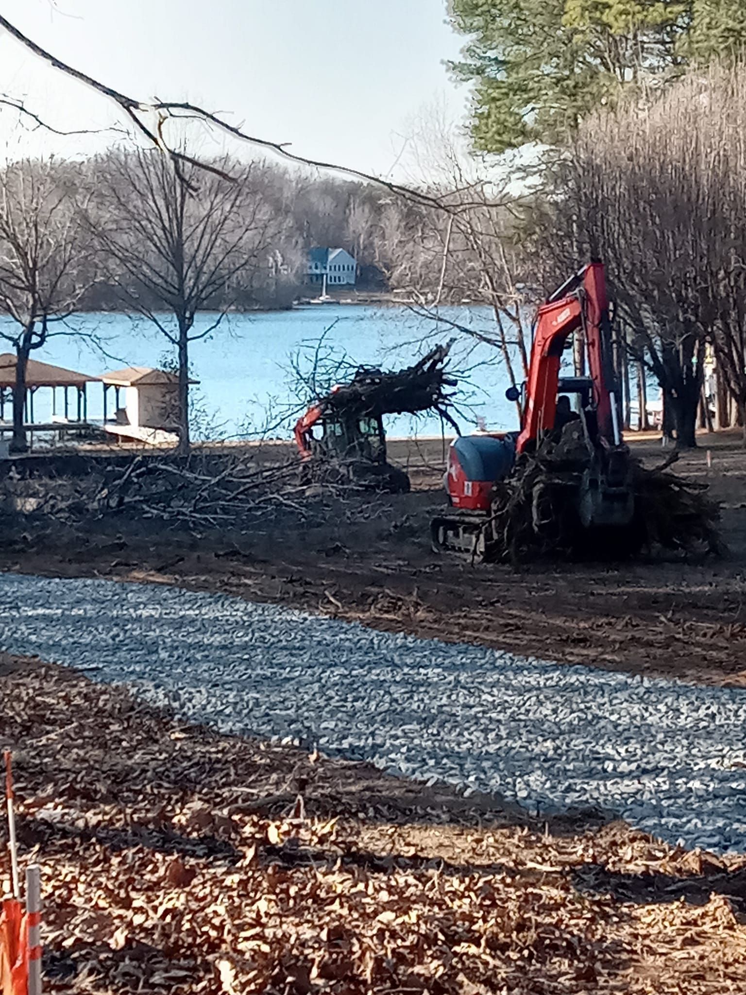 a red excavator is working on a dirt field next to a body of water .