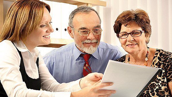Financial advisor reviewing paperwork with an older couple, smiles, indoor office setting.