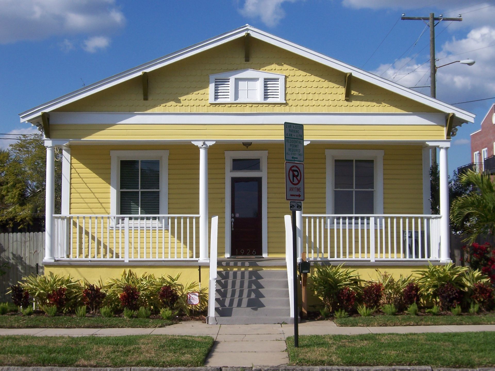 Yellow bungalow with white trim, porch, and a brown door; sunny day.
