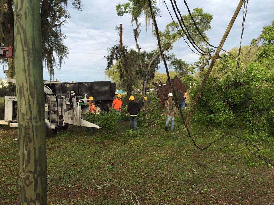 Overturned truck with crew in yellow/orange vests near downed power lines, cloudy day.