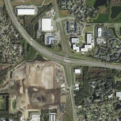 Aerial view of highway intersection and surrounding buildings and undeveloped land.