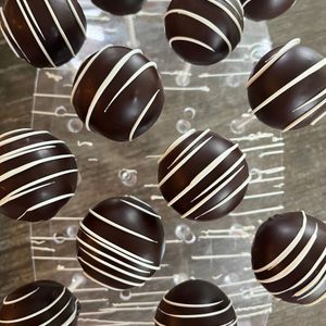Chocolate truffles with white drizzle arranged on a rustic wooden surface