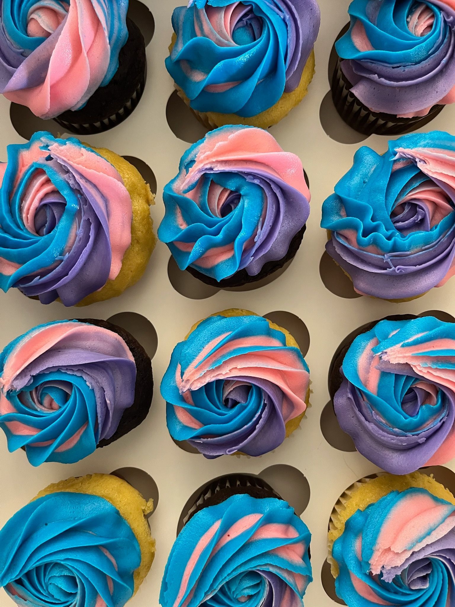 Colorful frosted cupcakes with blue, pink, and purple swirls arranged in a neat grid
