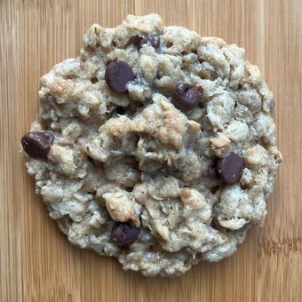A single chocolate chip oatmeal cookie on a wooden surface.