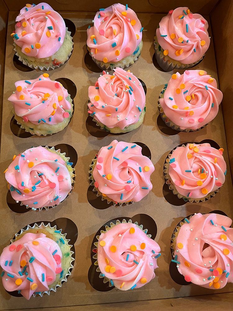 a box of cupcakes with pink frosting and sprinkles