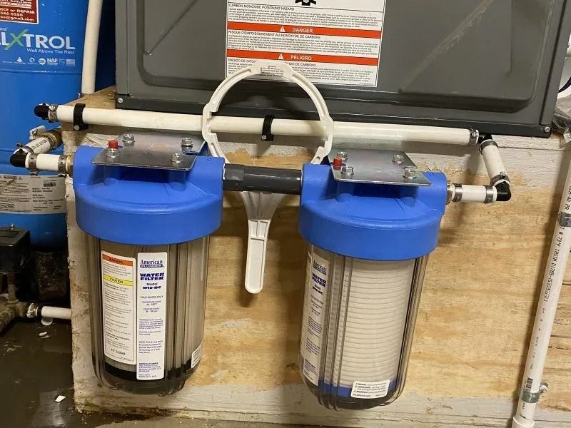 Two blue water filter housings connected to pipes, mounted on a wooden structure.