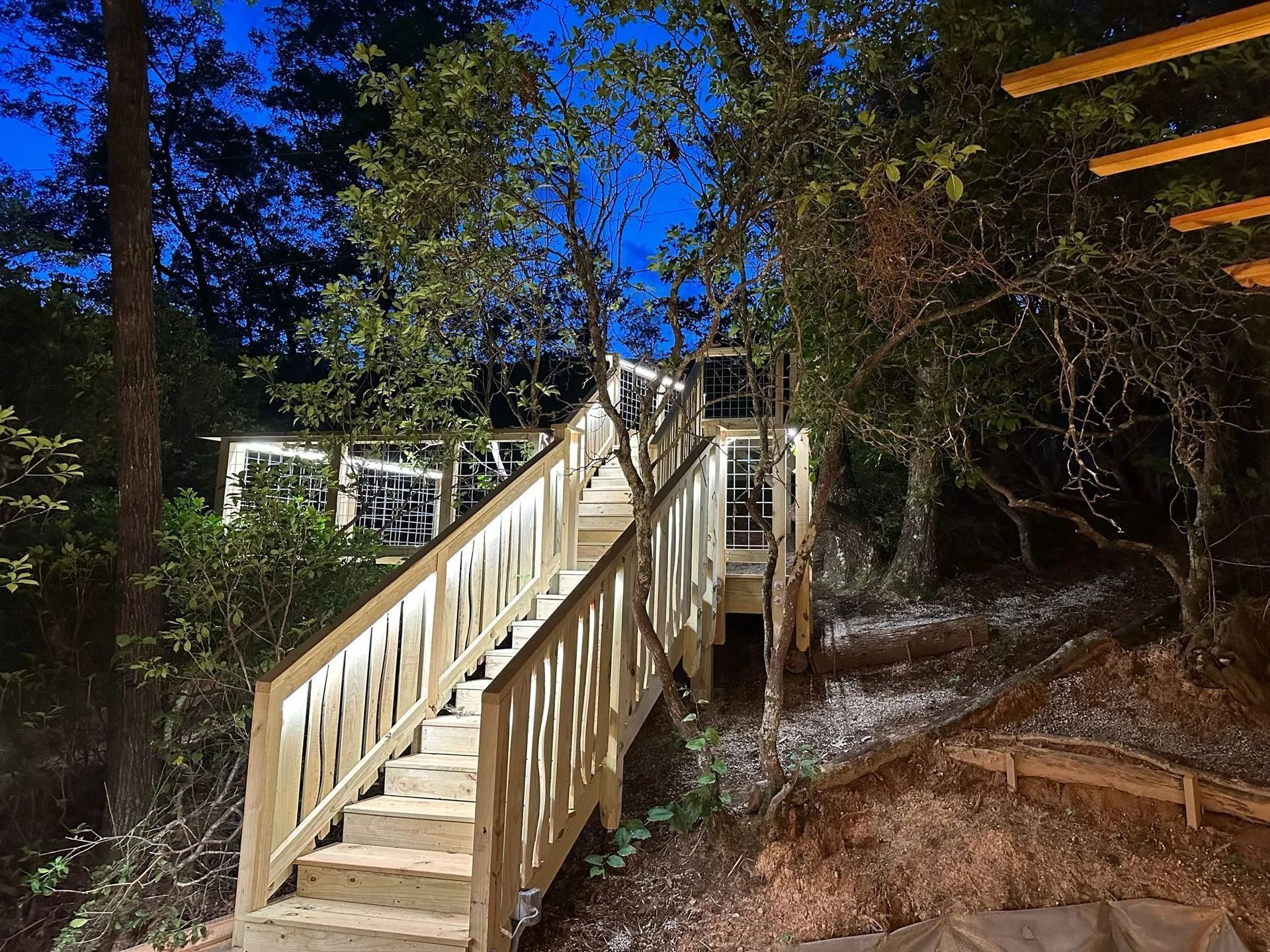 Wooden staircase lit up at night, leading to a cabin nestled in trees.