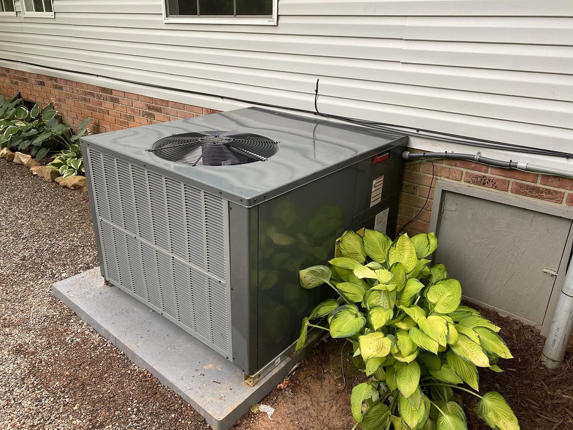 An outdoor air conditioning unit next to a house with small plants and a window.