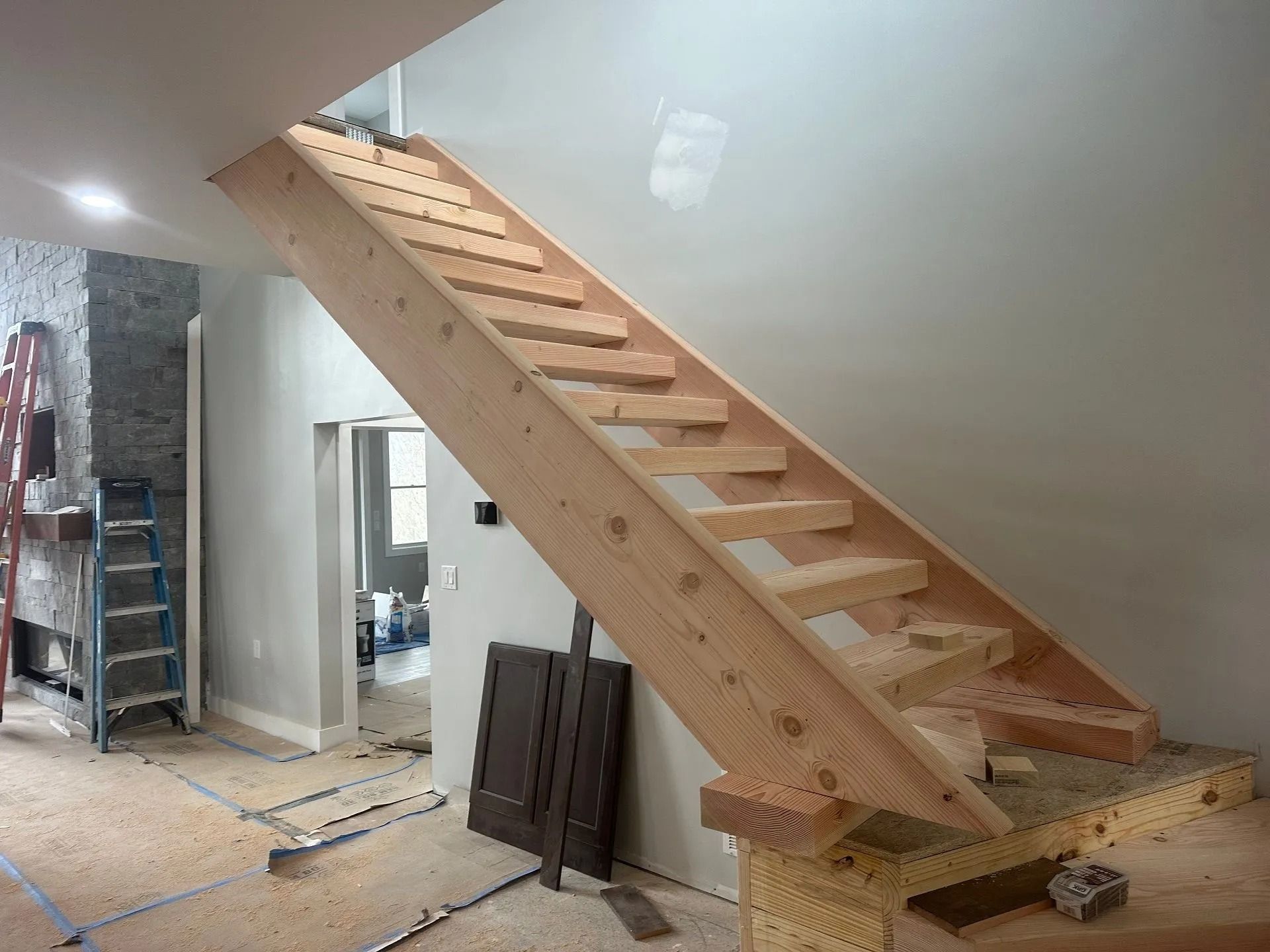 Unfinished wooden staircase with open risers, ascending against a light gray wall during home construction.