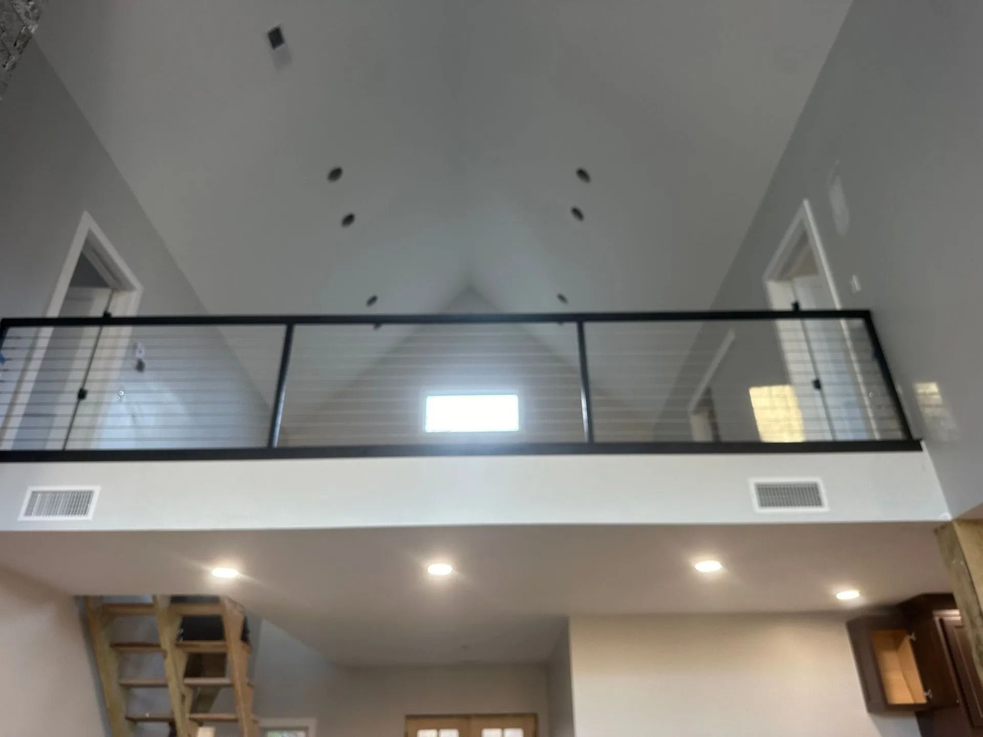 Interior view of a loft with a black railing and cable, recessed lights, and gray walls.