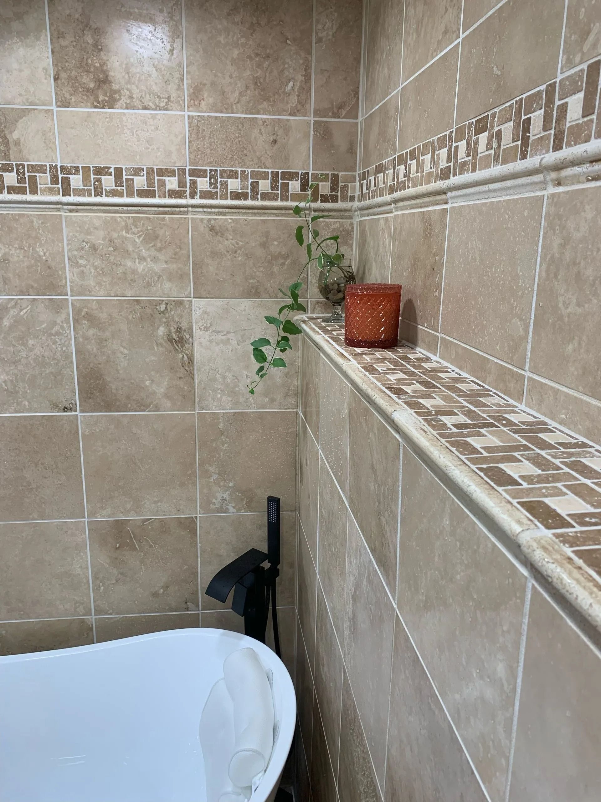 Tiled bathroom with a shelf holding a plant and a box. A white tub is in the lower left corner.