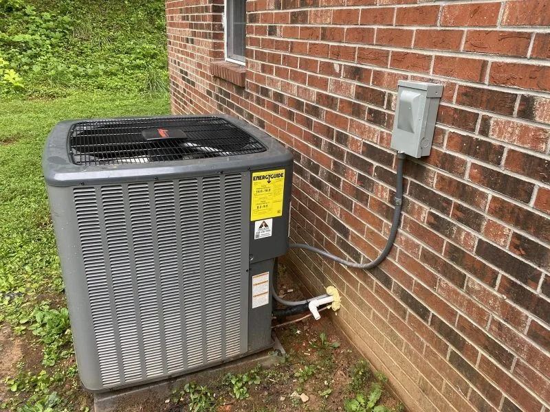 Air conditioner unit next to a brick building. Electrical box attached. Yellow sticker.