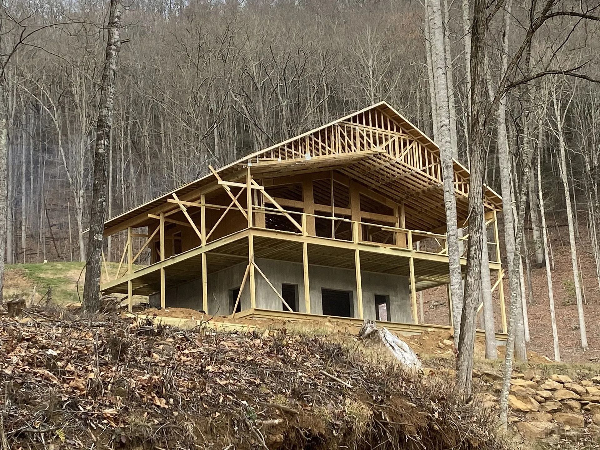 House under construction in a wooded area, with exposed wooden frame.