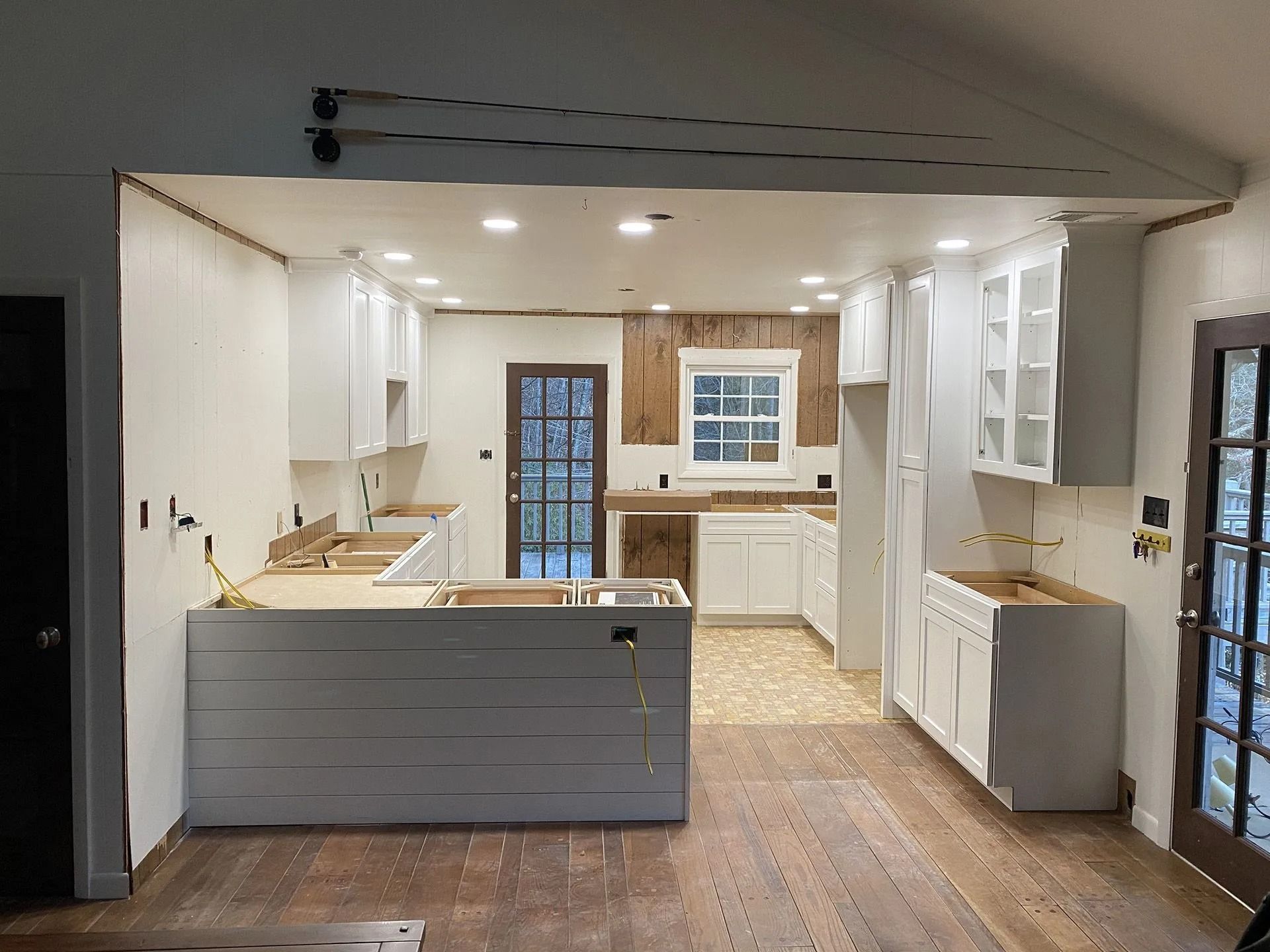 Kitchen renovation in progress: white cabinets, wood panel wall, island with shiplap, open doorway.