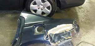 A damaged car fender is sitting next to a car in a garage