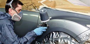 A man wearing a mask and gloves is spray painting a car