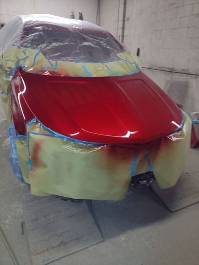 Red car body in a workshop, taped off and partially painted with red and beige primer.