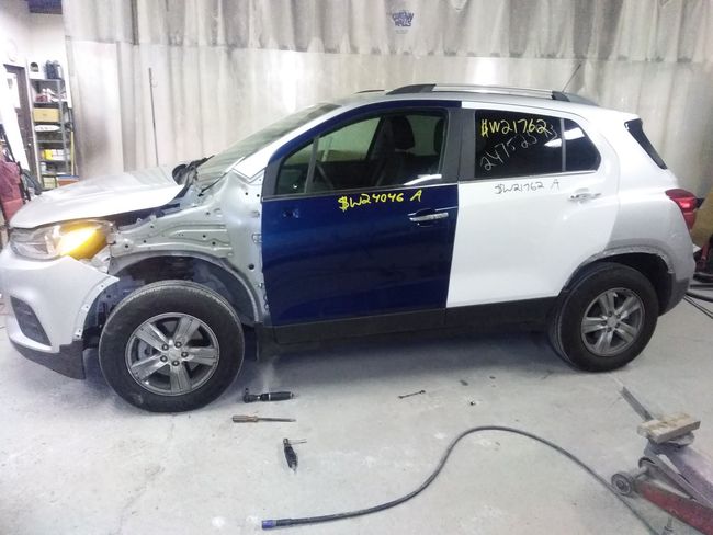 A blue and white car is being painted inside an auto shop