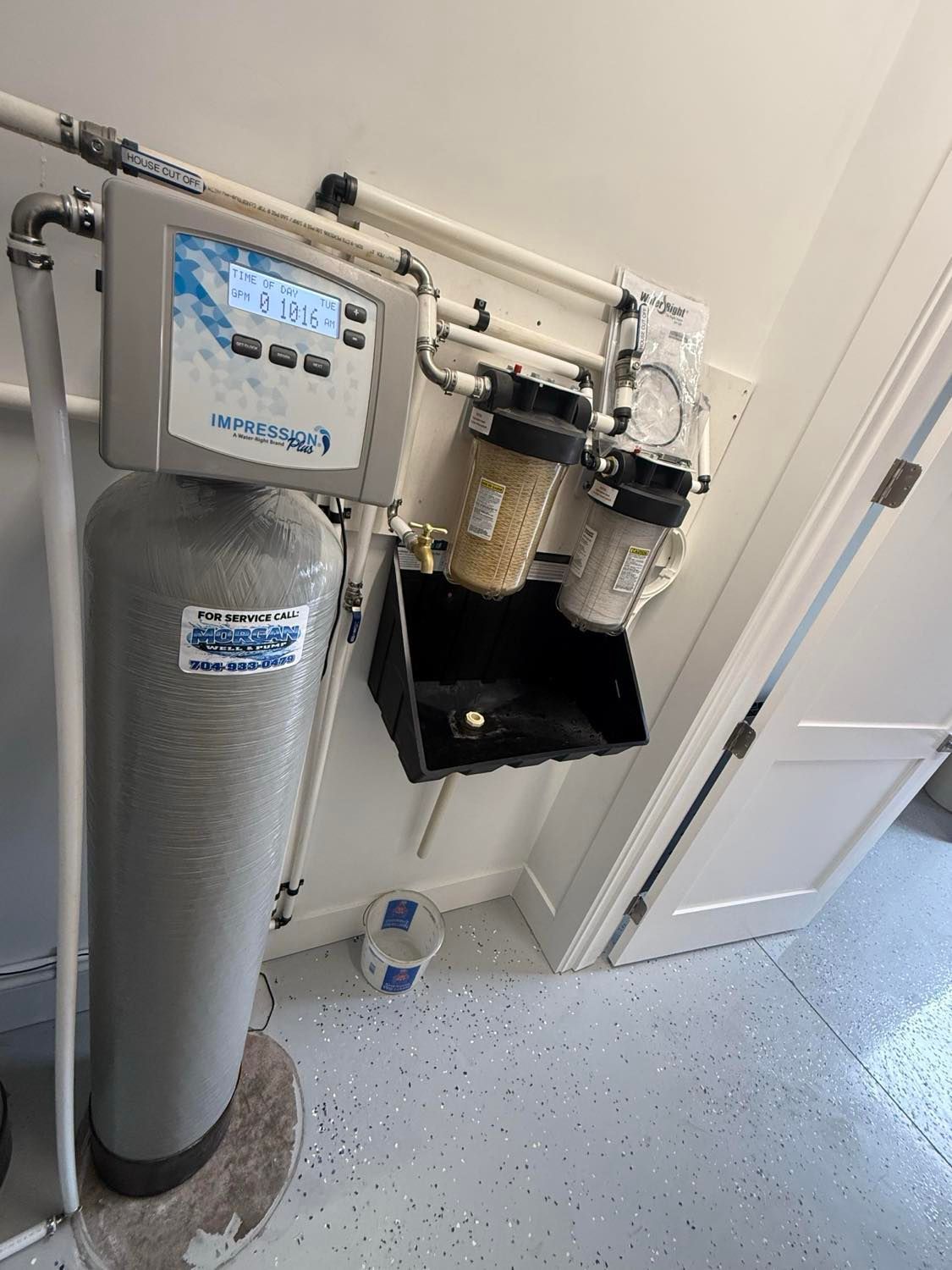 Water filtration system with a large grey tank and two smaller wall-mounted filters in a utility room.