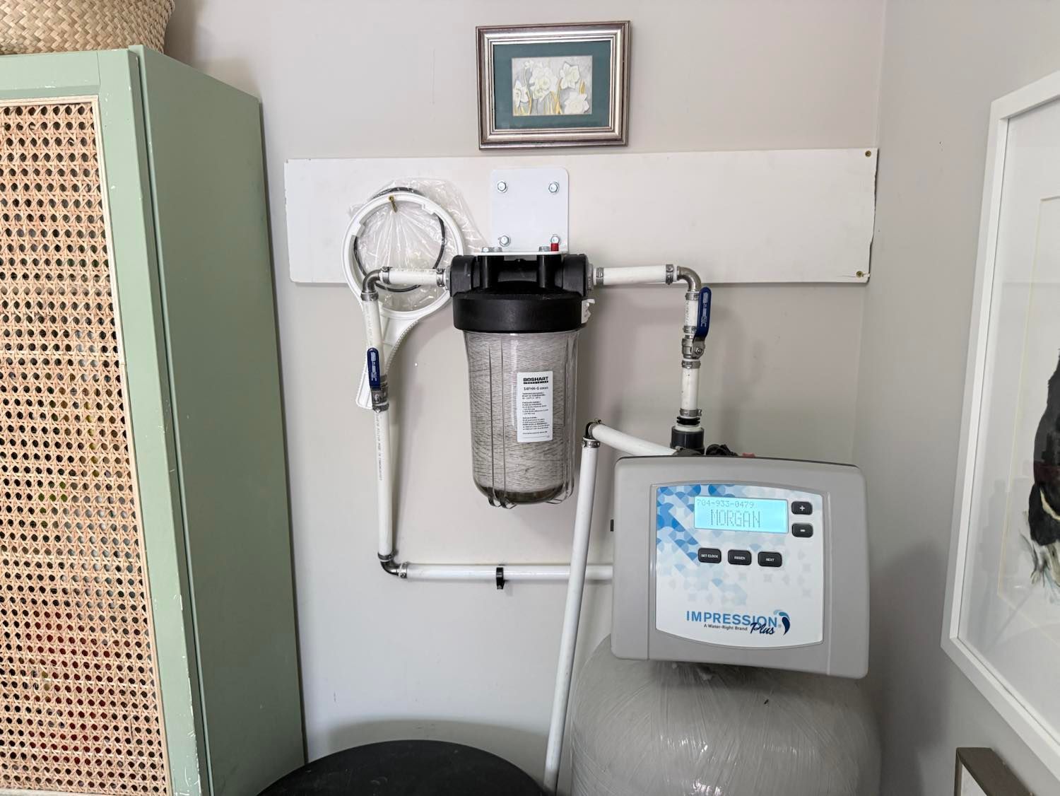 A water filtration system mounted on a wall, featuring a black filter housing and a digital control unit on a grey tank.