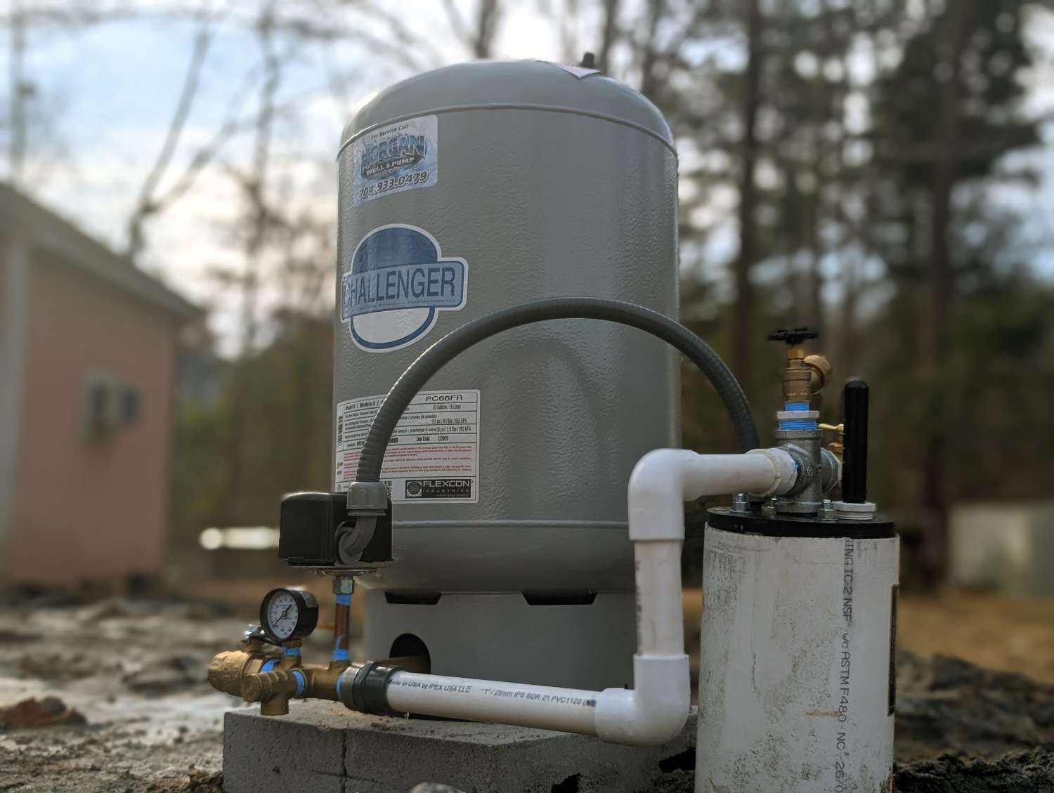 A grey Challenger well pressure tank and pump system installed on concrete blocks outdoors.