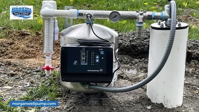 A Grundfos solar well pump controller mounted on a stainless steel pressure tank, positioned outdoors on bare ground.