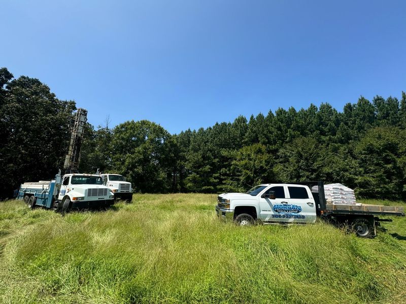 Two service trucks parked in a grassy field surrounded by trees under a clear blue sky.