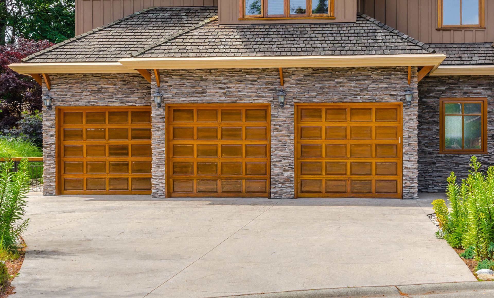 A large house with three wooden garage doors and a stone wall.