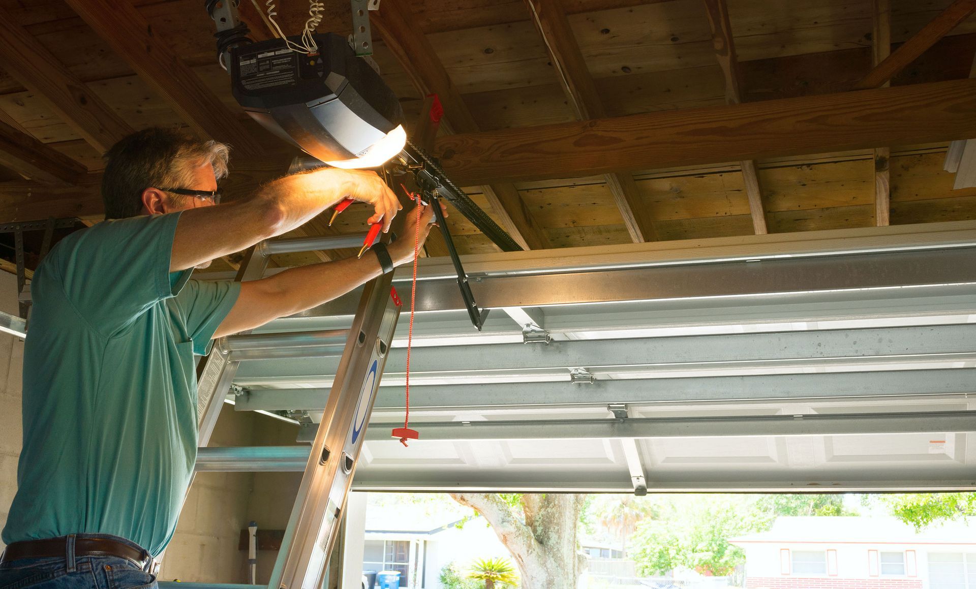 A man is using a ladder to fix a garage door opener.