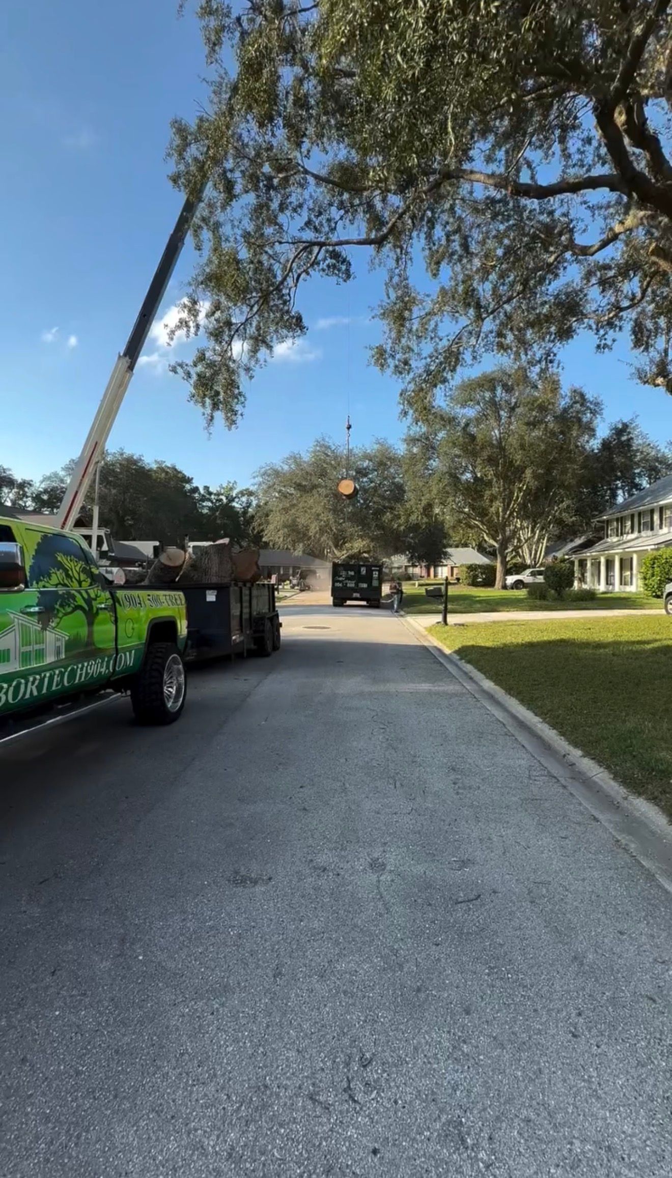 Tree-trimming truck on a quiet suburban street with a bucket lift and work area coned off.