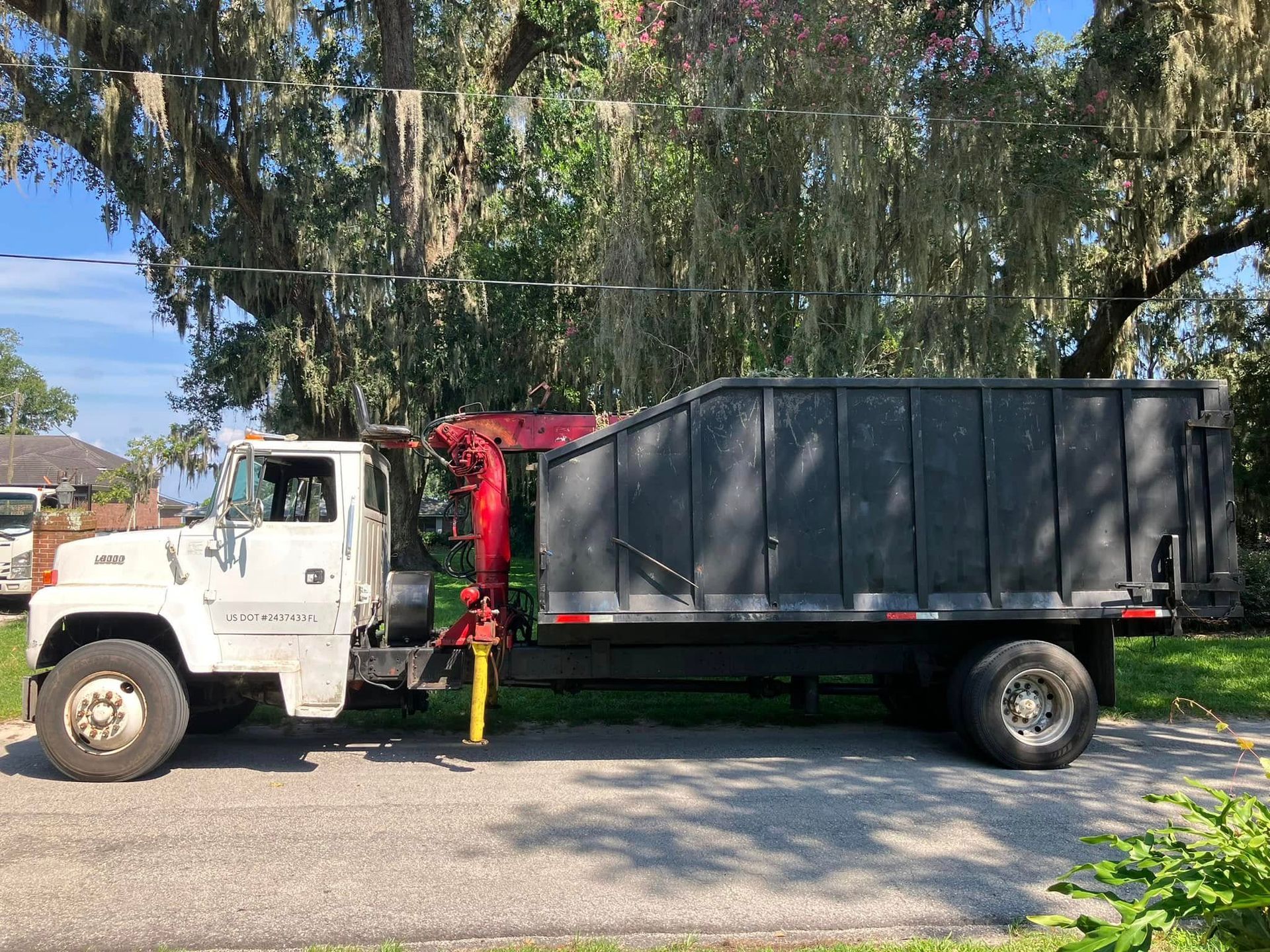 White cab truck with black cargo bed parked on a street under trees, side view.