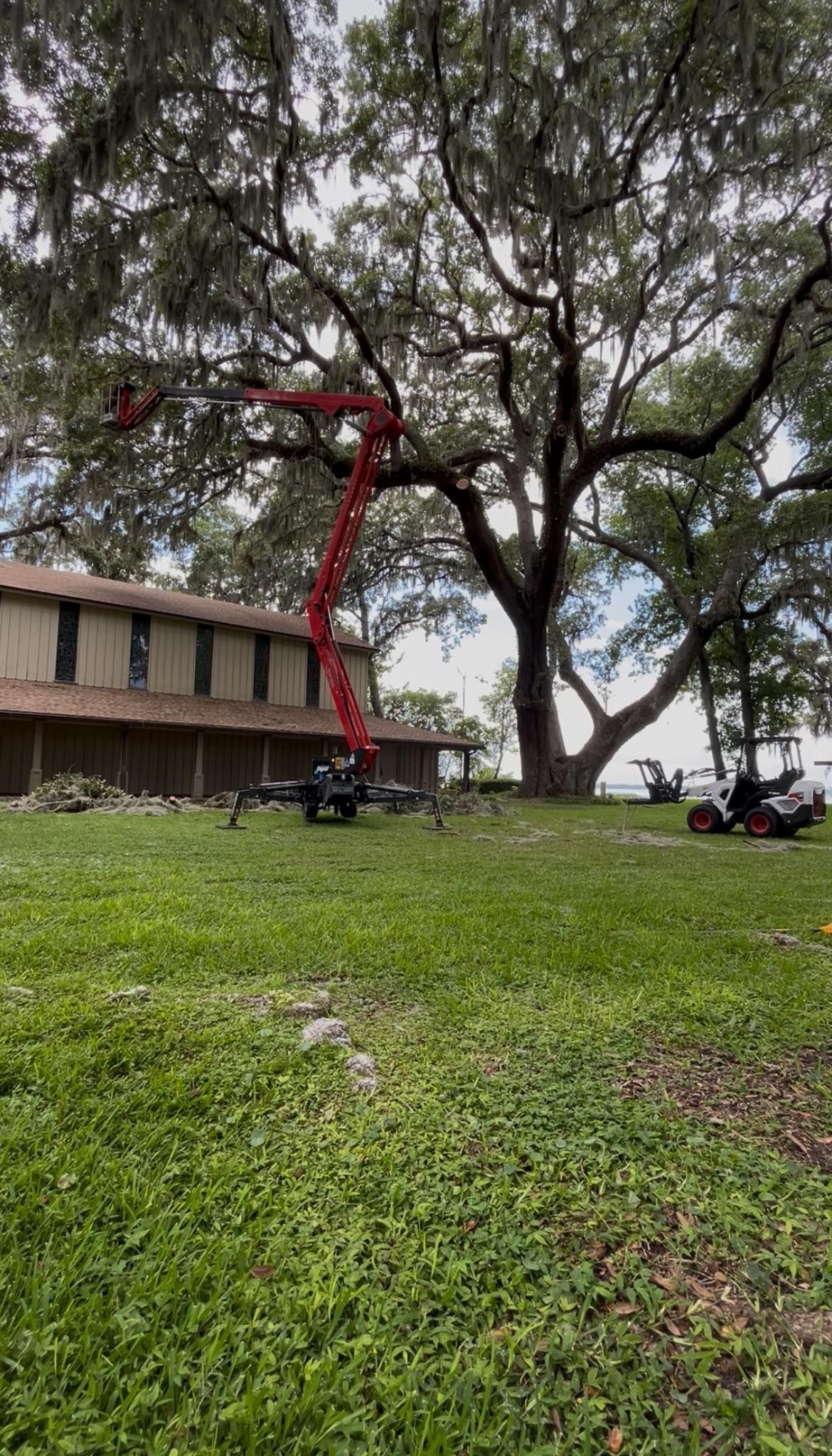 Red cherry picker beside a building under large trees on a grassy lawn.