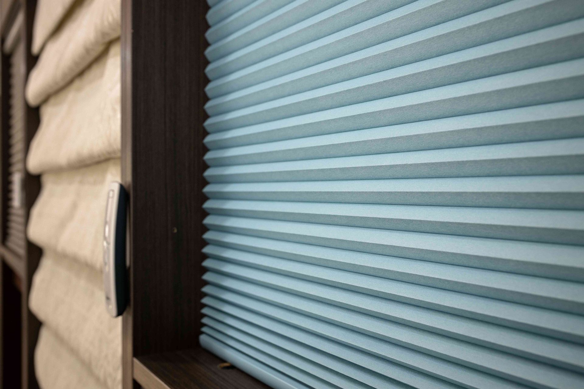 Window with beige blinds beside a blue pleated shade and dark wood trim
