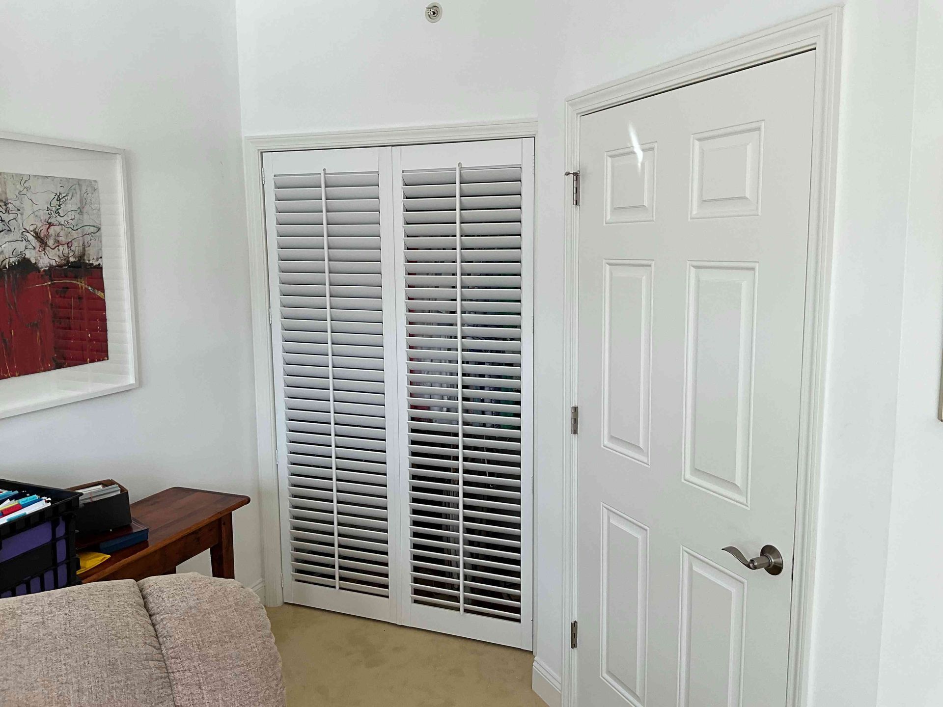 Bright room with white closet doors, a white door, and a small desk beside a beige sofa.