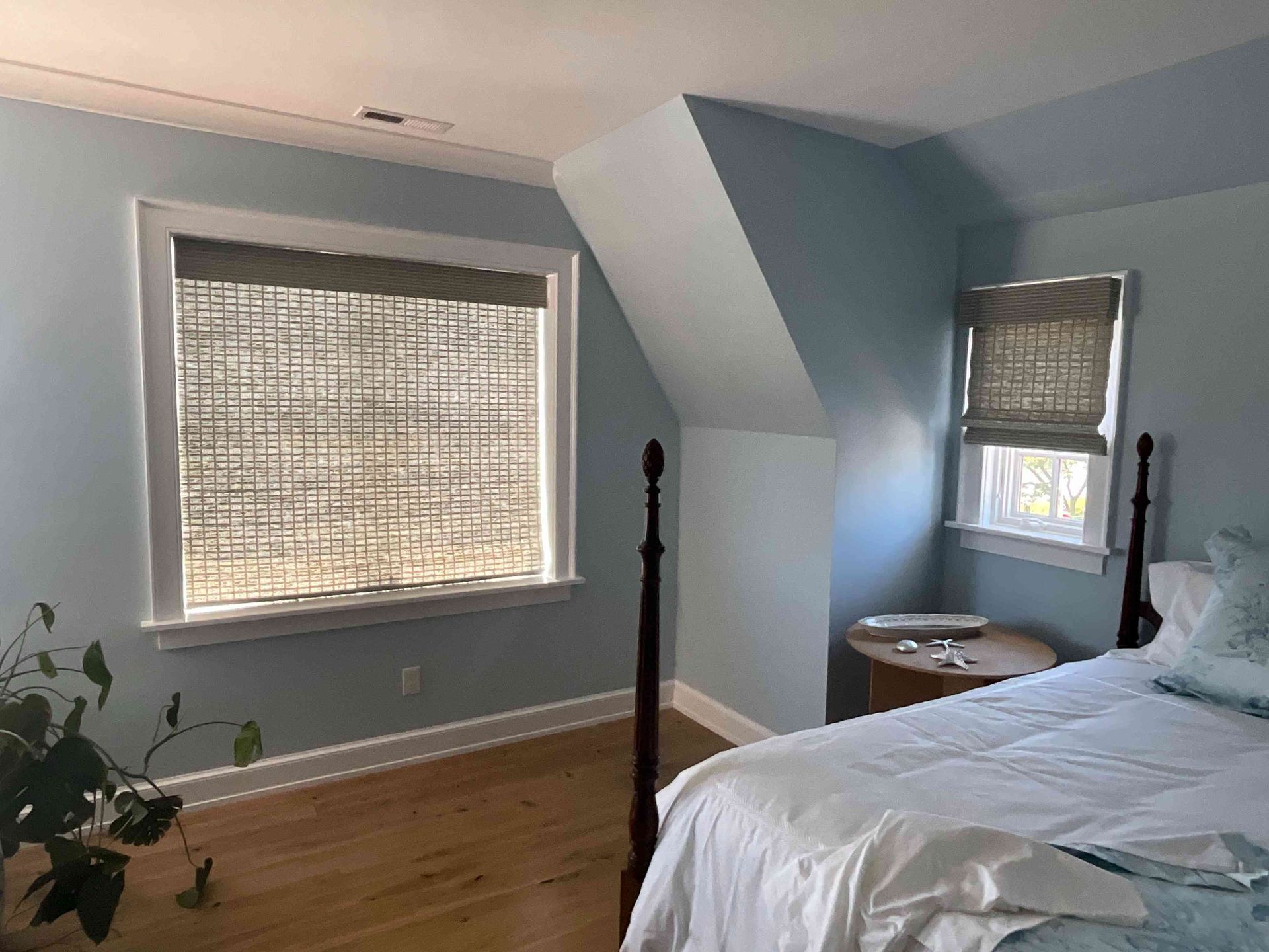 Bedroom with sloped ceiling, large window, bamboo blinds, and a bed with white bedding.