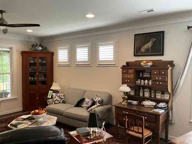 Bright living room with a gray sofa, wooden cabinets, shutters, and framed art on the walls