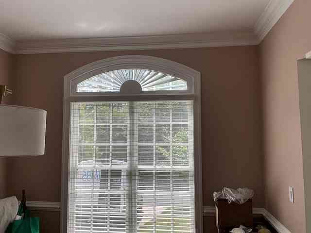 Sunlit bedroom with arched window, white blinds, beige walls, and a small wooden nightstand