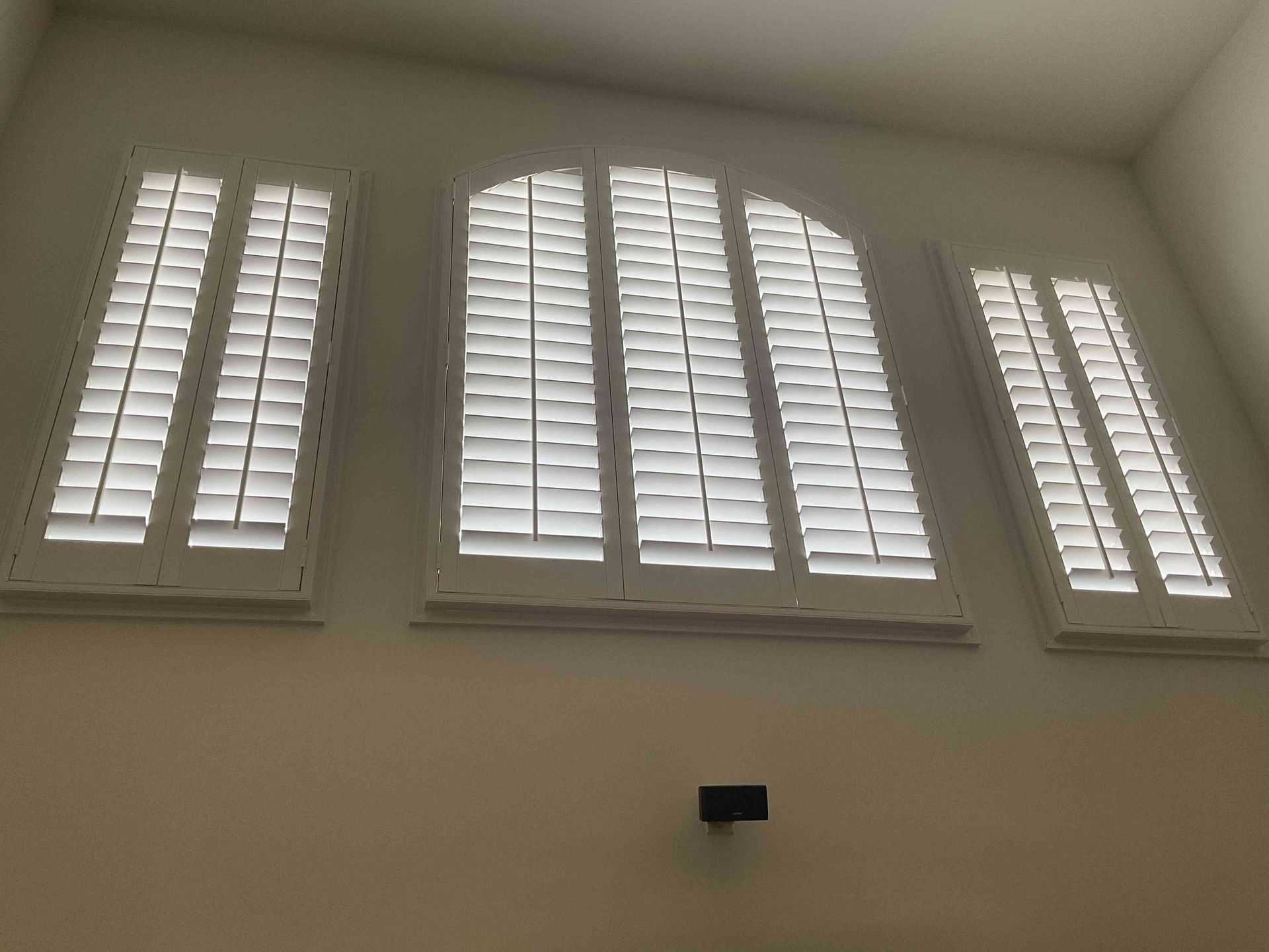 Tall white shuttered windows on a wall in a bright room, viewed from below.