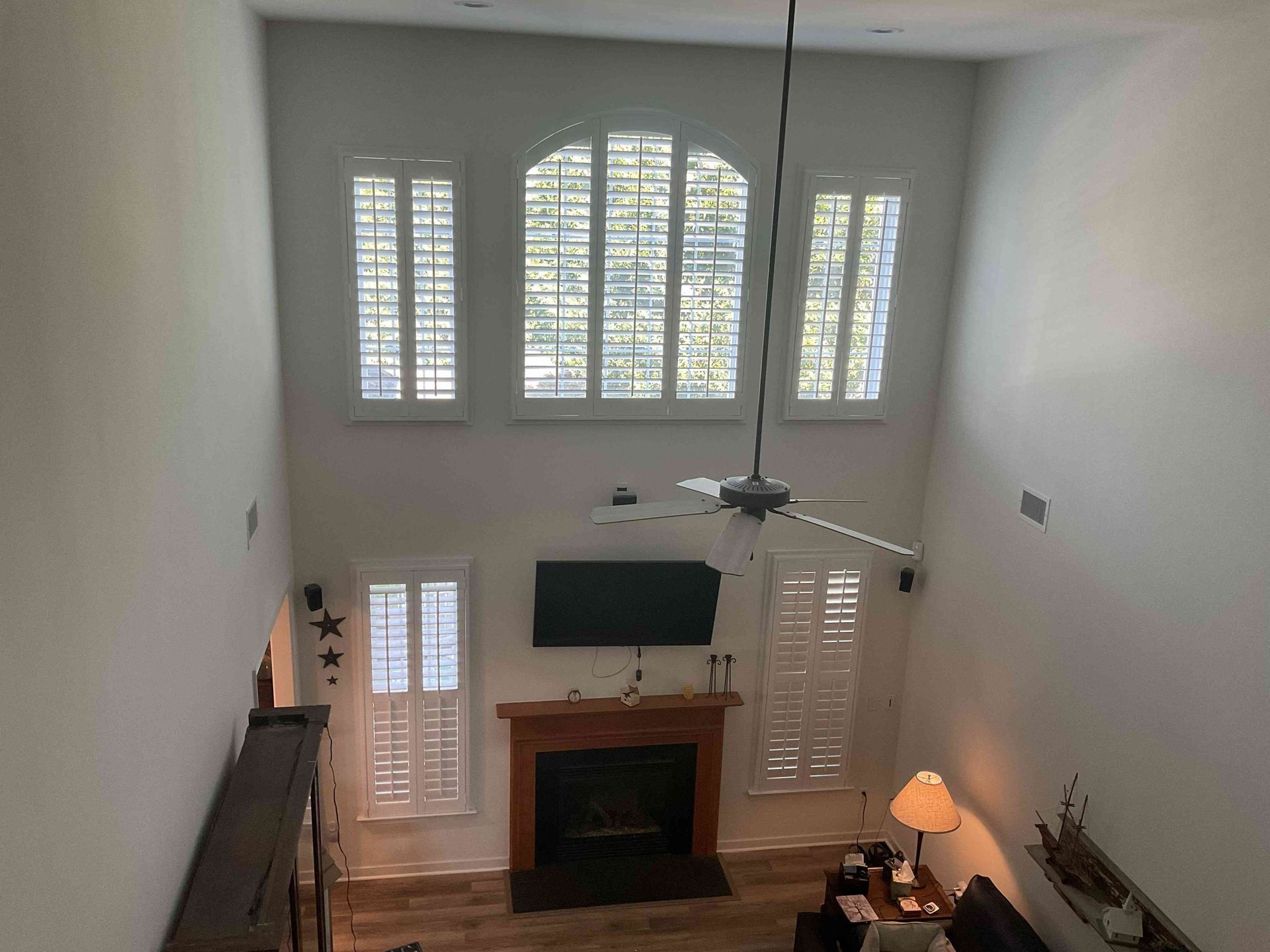 Bright living room with high windows, fireplace, ceiling fan, and a wall-mounted TV under a vaulted ceiling