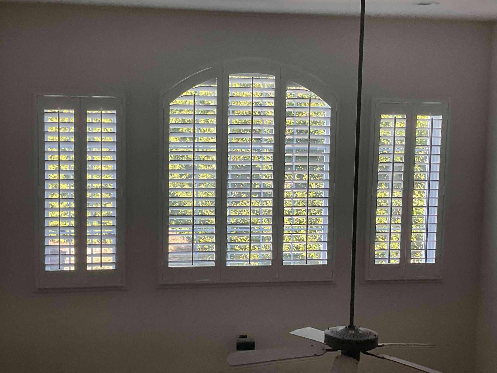 White window shutters in a room, with an arched center window and a small table lamp below.
