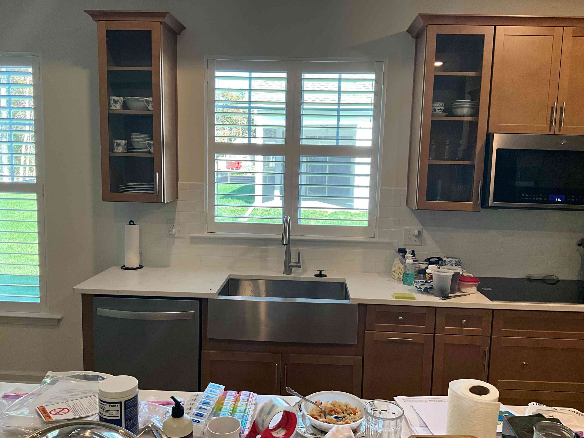 Kitchen with sink under a window, wooden cabinets, and cluttered counters in the foreground