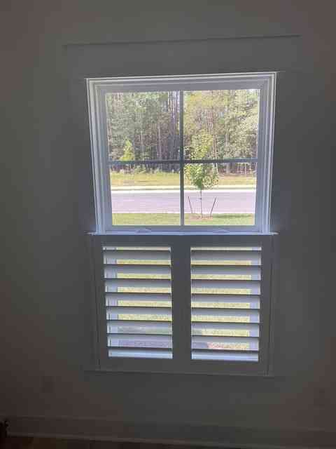 Window with a view of a road and trees, with shutters on the lower half