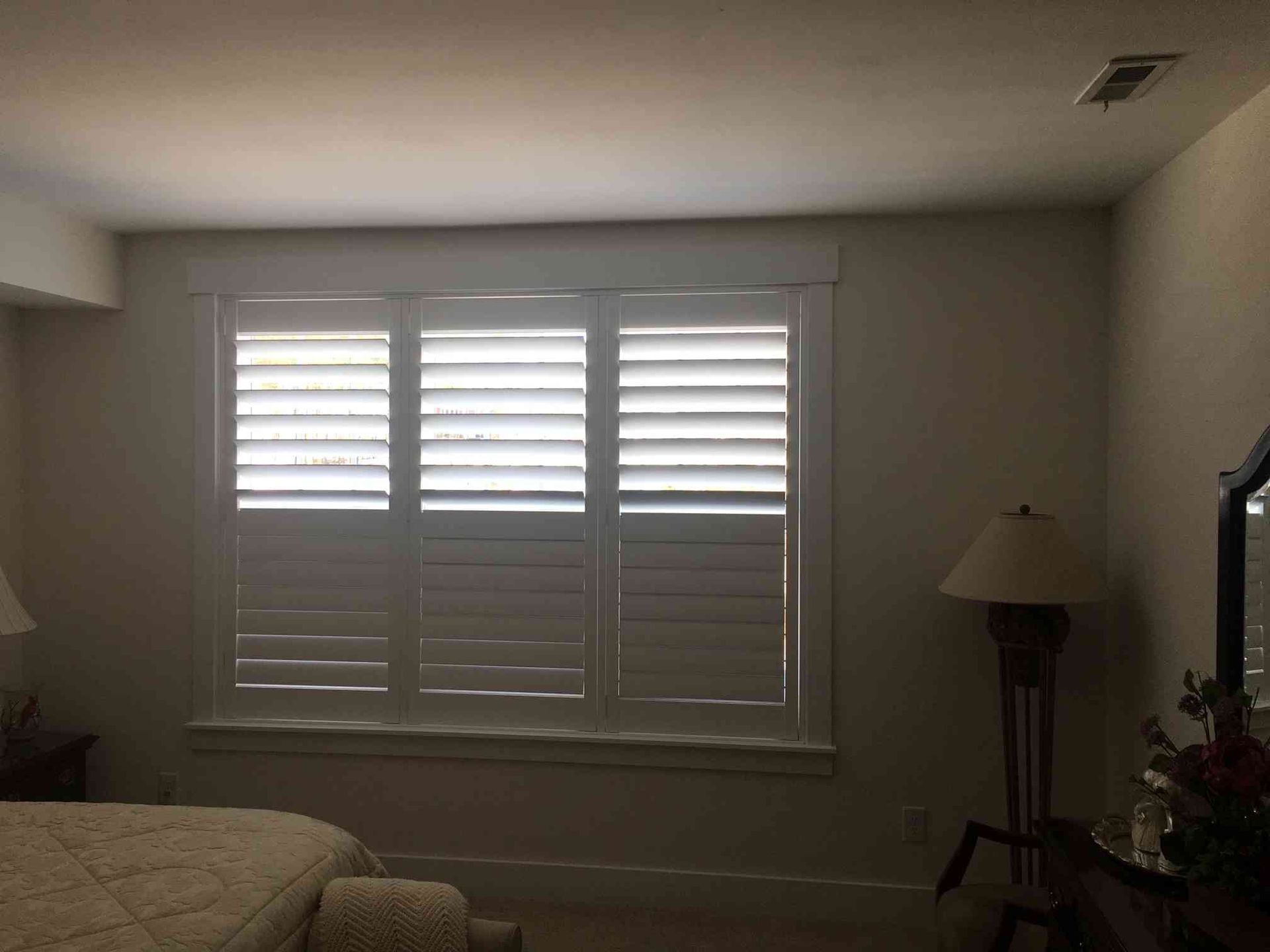 Dim bedroom with a shuttered window, bed corner, floor lamp, and TV in the background.