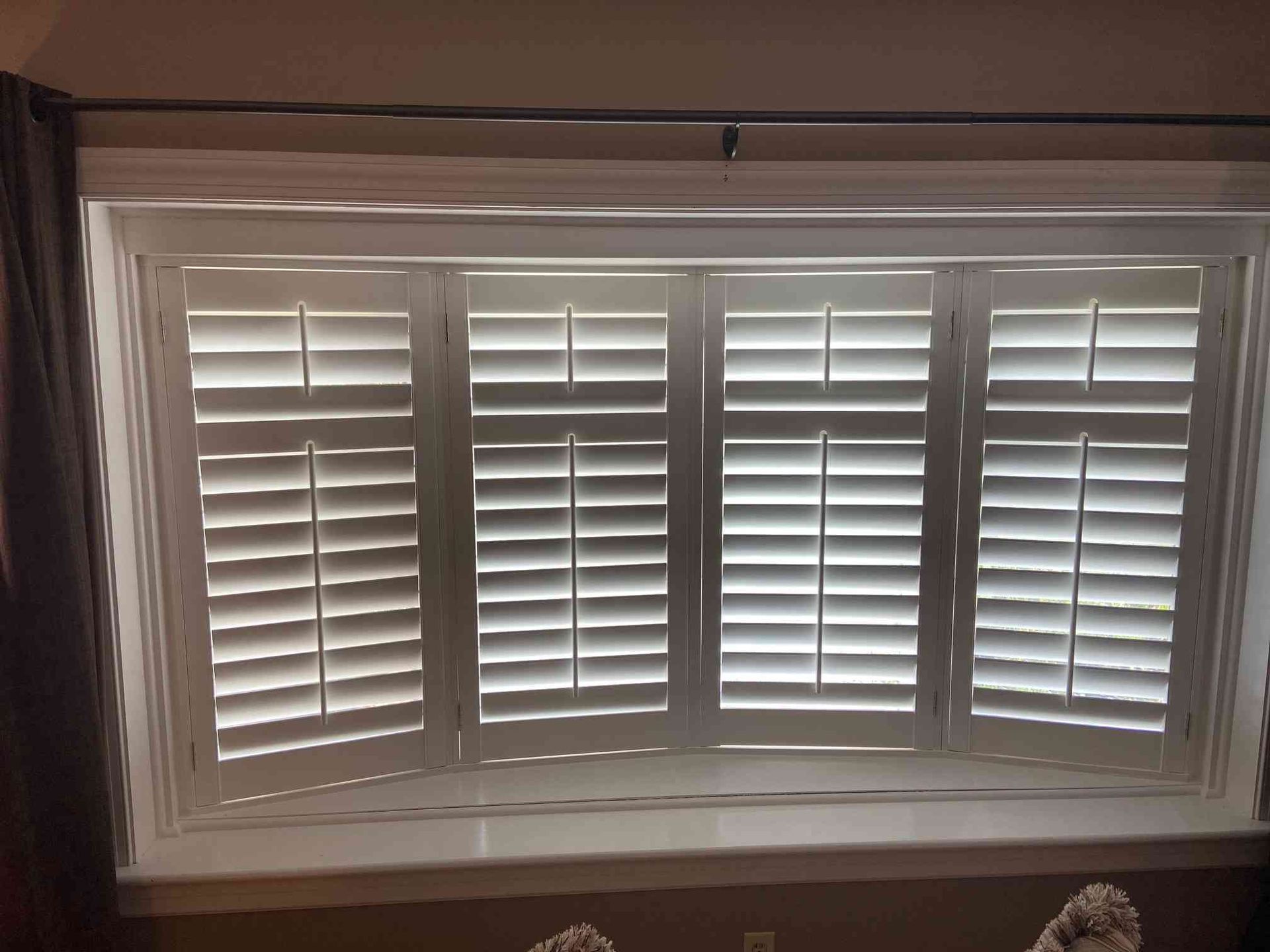White plantation shutters on a bay window with daylight filtering through slats