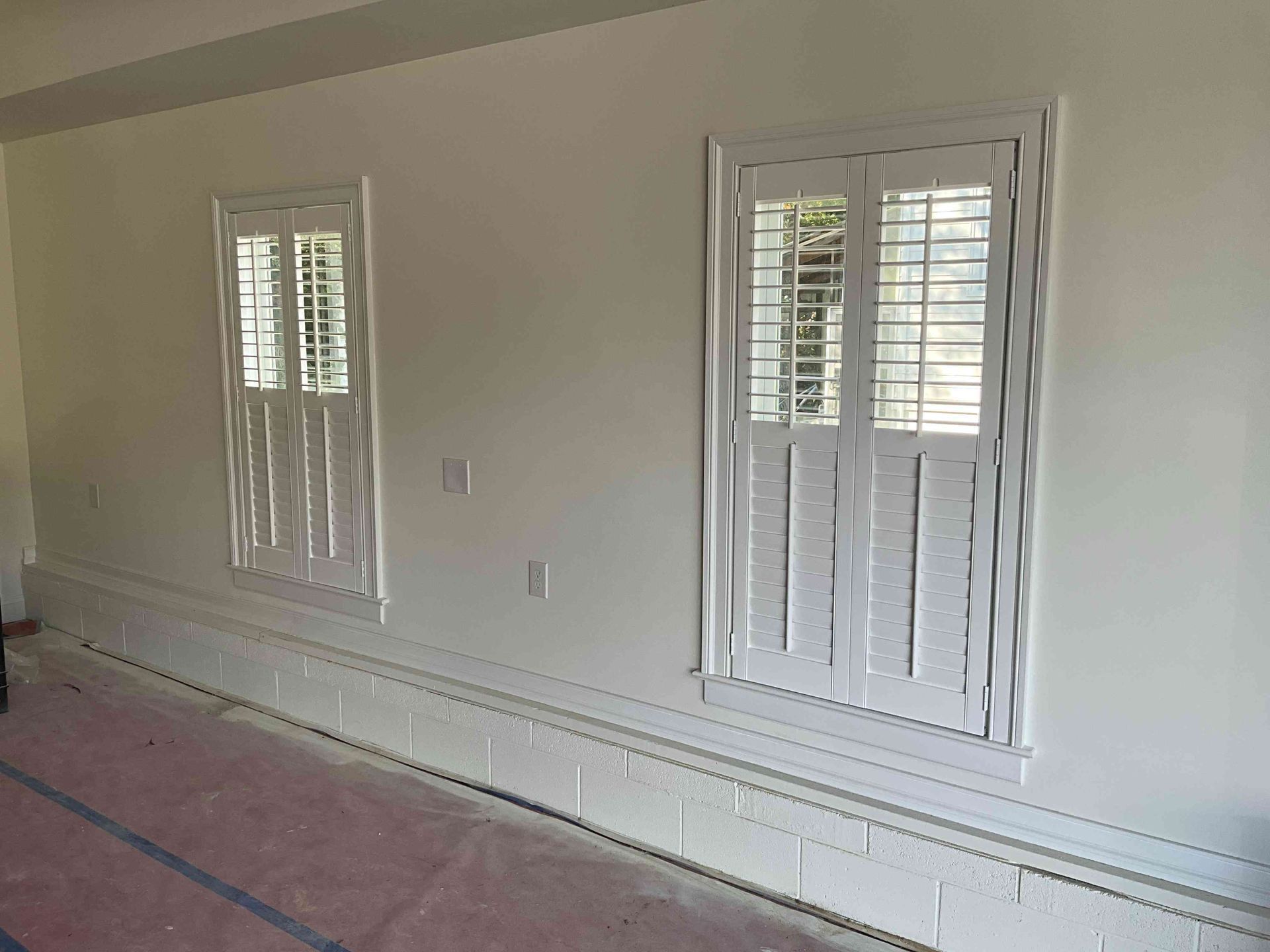 Empty room with white walls, shuttered windows, and carpet laid for installation or renovation