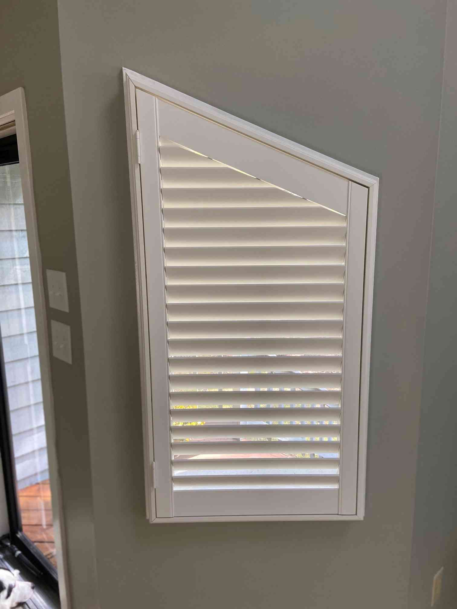White louvered window shutter in a gray interior wall panel